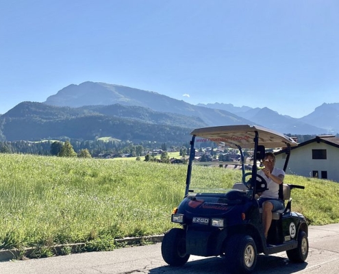 E-Golfcart von Ferienwohnungen Neumaier in Reit im Winkl, Christa Neumaier in Golfcart, Bergpanorama im Hintergrund